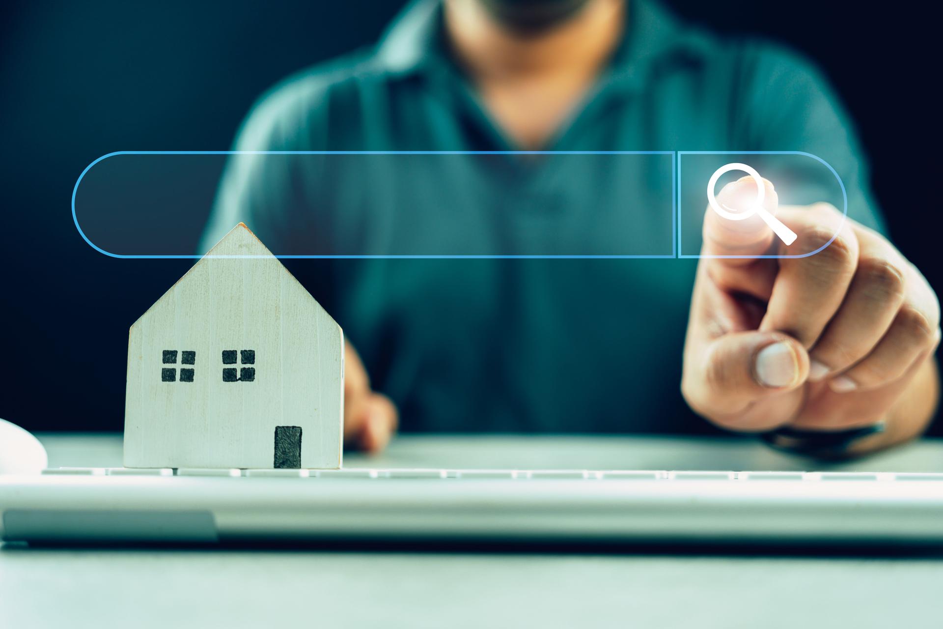 Man clicking internet search page on touch screen with wood home on keyboard. Search advertising for rent or buy a home.